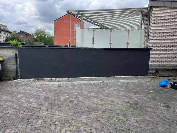 Dieselbe Hofmauer nach der Arbeit: gleichmäßig dunkel gestrichen, Hof geräumt