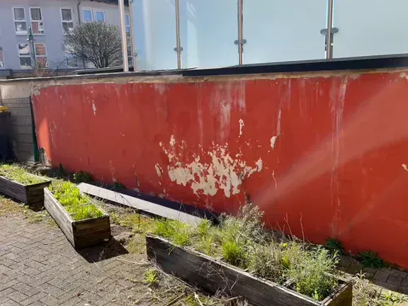 Hofmauer vorher: rote Farbe blättert großflächig ab, davor alte Hochbeete